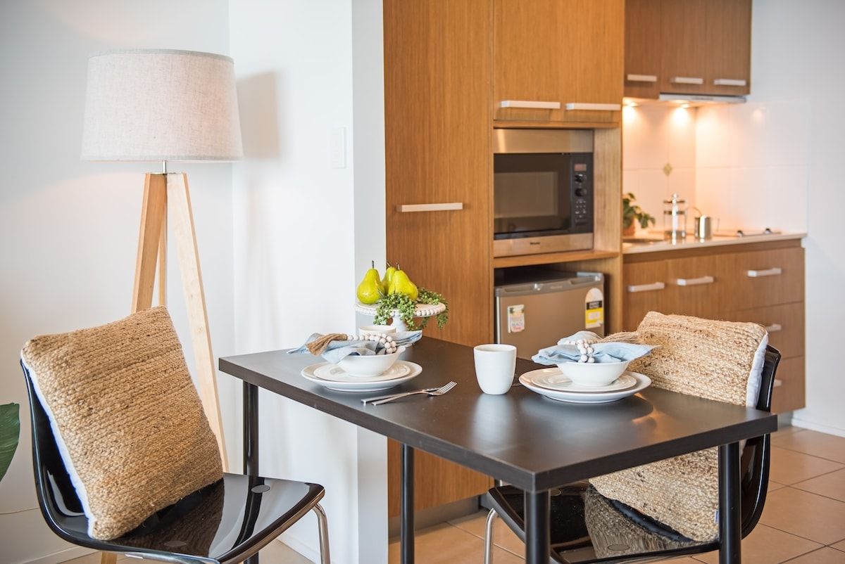 Una cucina moderna con mobili in legno, un forno a microonde e un tavolo da pranzo apparecchiato con piatti, ciotole e una tazza.