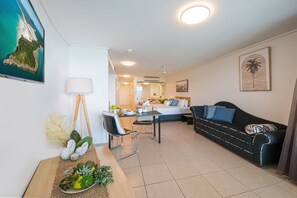 A modern living room with a sofa, a dining table, and a TV displaying a scenic view. - Ocean Dreams Studio Apartment On Airlie (Airlie Beach)