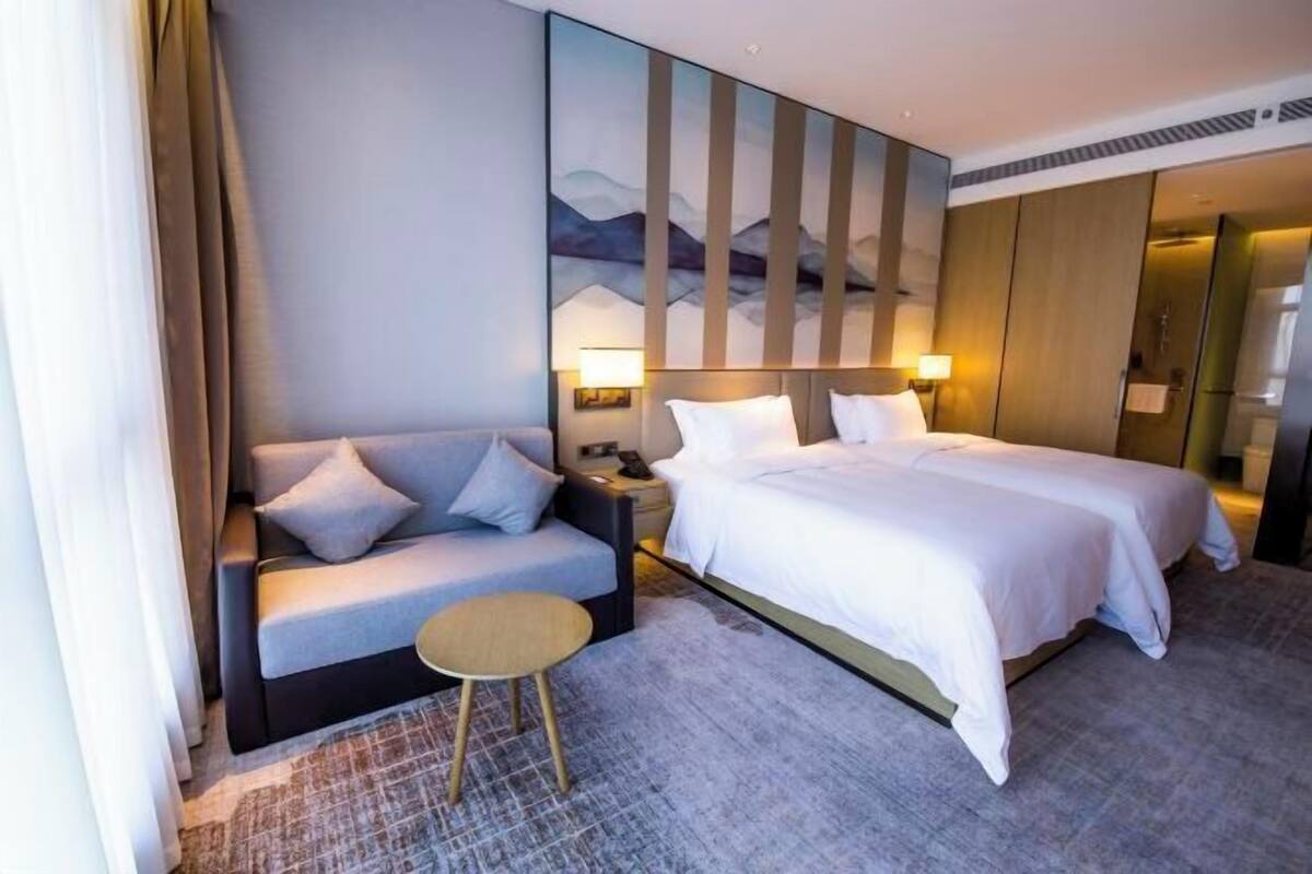 A hotel room with a bed, a sofa, a small table, and a painting on the wall.