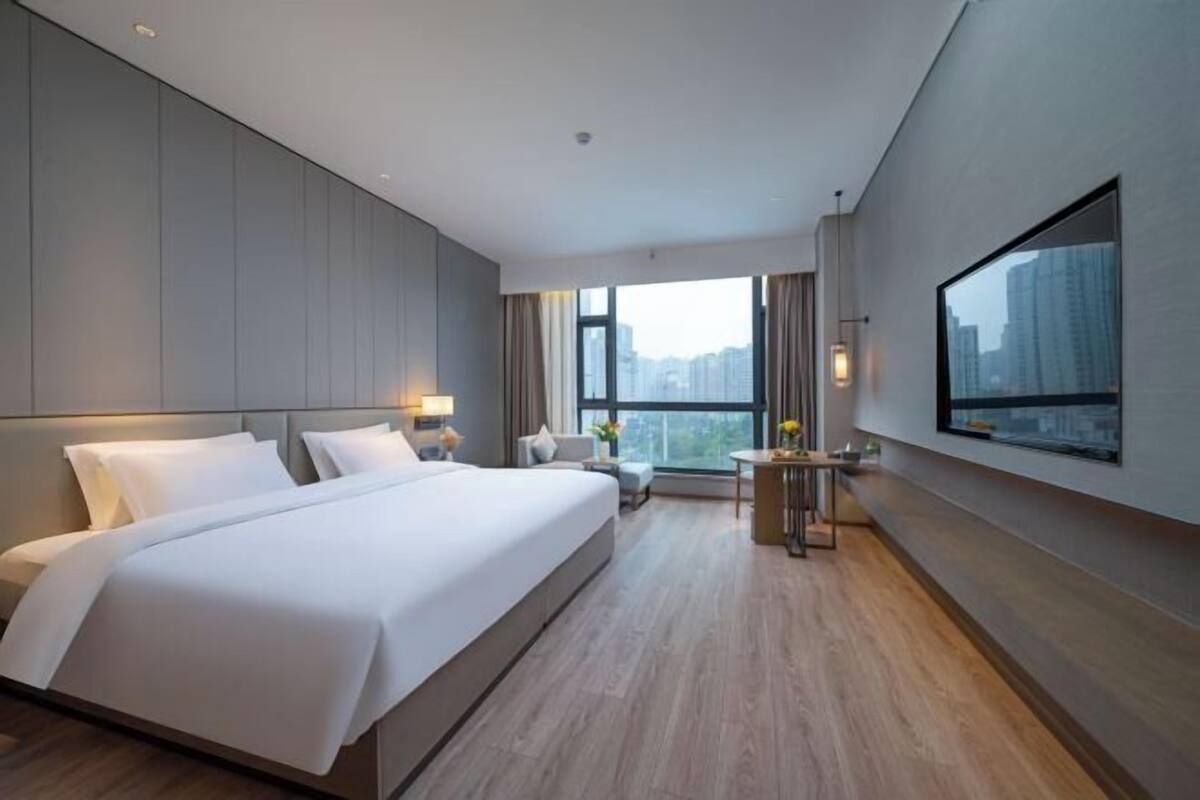 A modern hotel room with a large bed, a desk, and a city view.