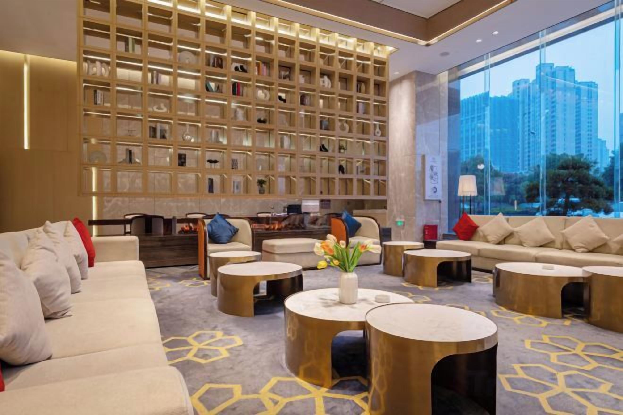 A modern hotel lobby with a large bookshelf, comfortable seating, and a view of the city.