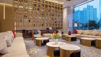 A modern hotel lobby with a large bookshelf, comfortable seating, and a view of the city.