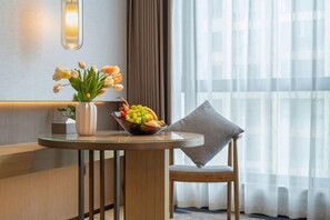 Quarto de hotel com uma mesa redonda, um vaso de flores e uma cesta de frutas.
