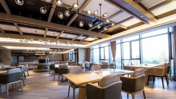 Un restaurante moderno con techos altos, iluminación colgante y grandes ventanales con vistas a la ciudad.
