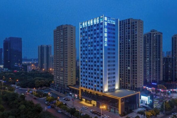 A high-rise hotel with illuminated signage, surrounded by other tall buildings, featuring a prominent entrance with a modern design. - Huake Xinyi Hotel (Zhuzhou)