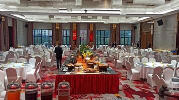 A banquet hall with round tables, a buffet table, and a person standing near the buffet.