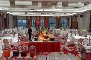 Una sala da banchetti con tavoli rotondi, un tavolo per il buffet e una persona in piedi vicino al buffet.