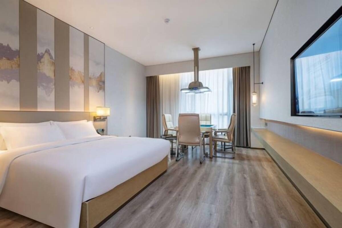 A hotel room with a large bed, a dining area with chairs, a table, and a large window.