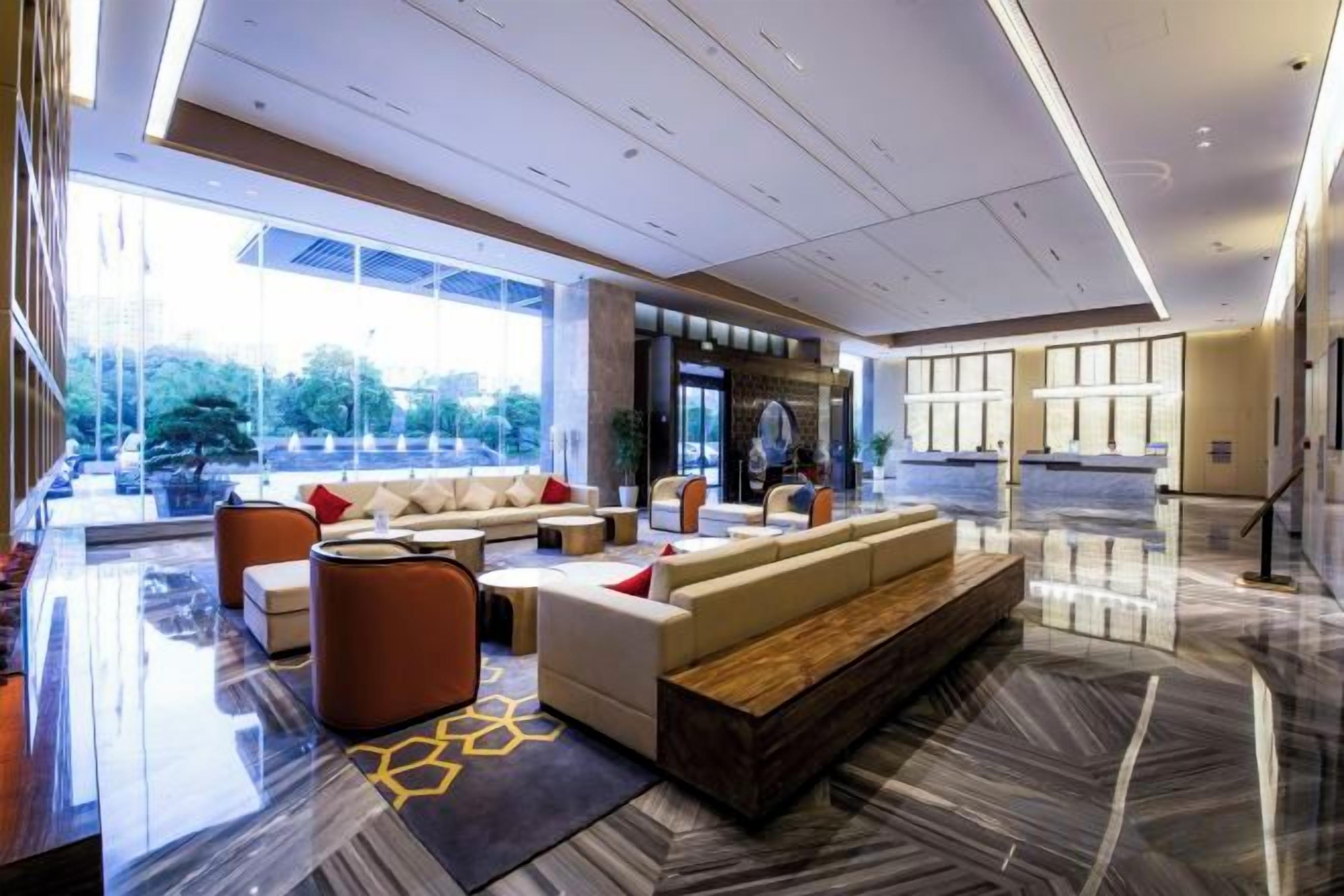 A modern hotel lobby with a seating area, a reception desk, and large windows offering a view of the outdoors.