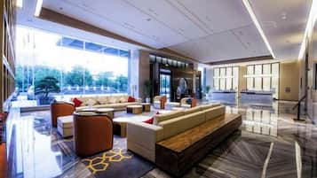 A modern hotel lobby with a seating area, a reception desk, and large windows offering a view of the outdoors.
