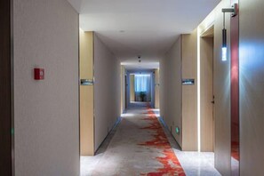 Pasillo de hotel con alfombra roja, puertas a ambos lados y un cartel que indica la dirección al ascensor.