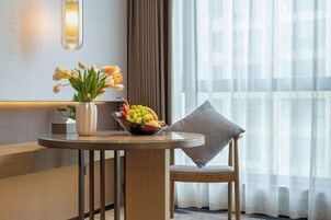 Una habitación de hotel con una mesa redonda, un florero, un frutero y una silla con cojín.