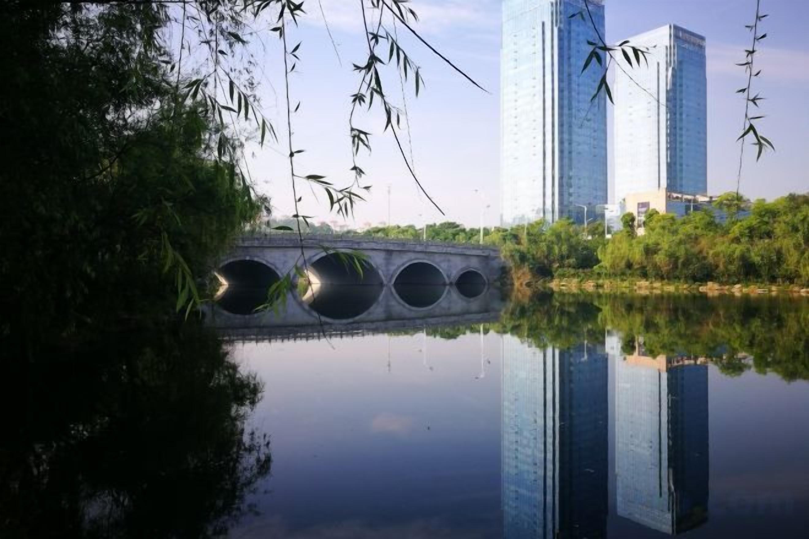 Un pont enjambant une étendue d’eau calme, avec un bâtiment moderne en arrière-plan.
