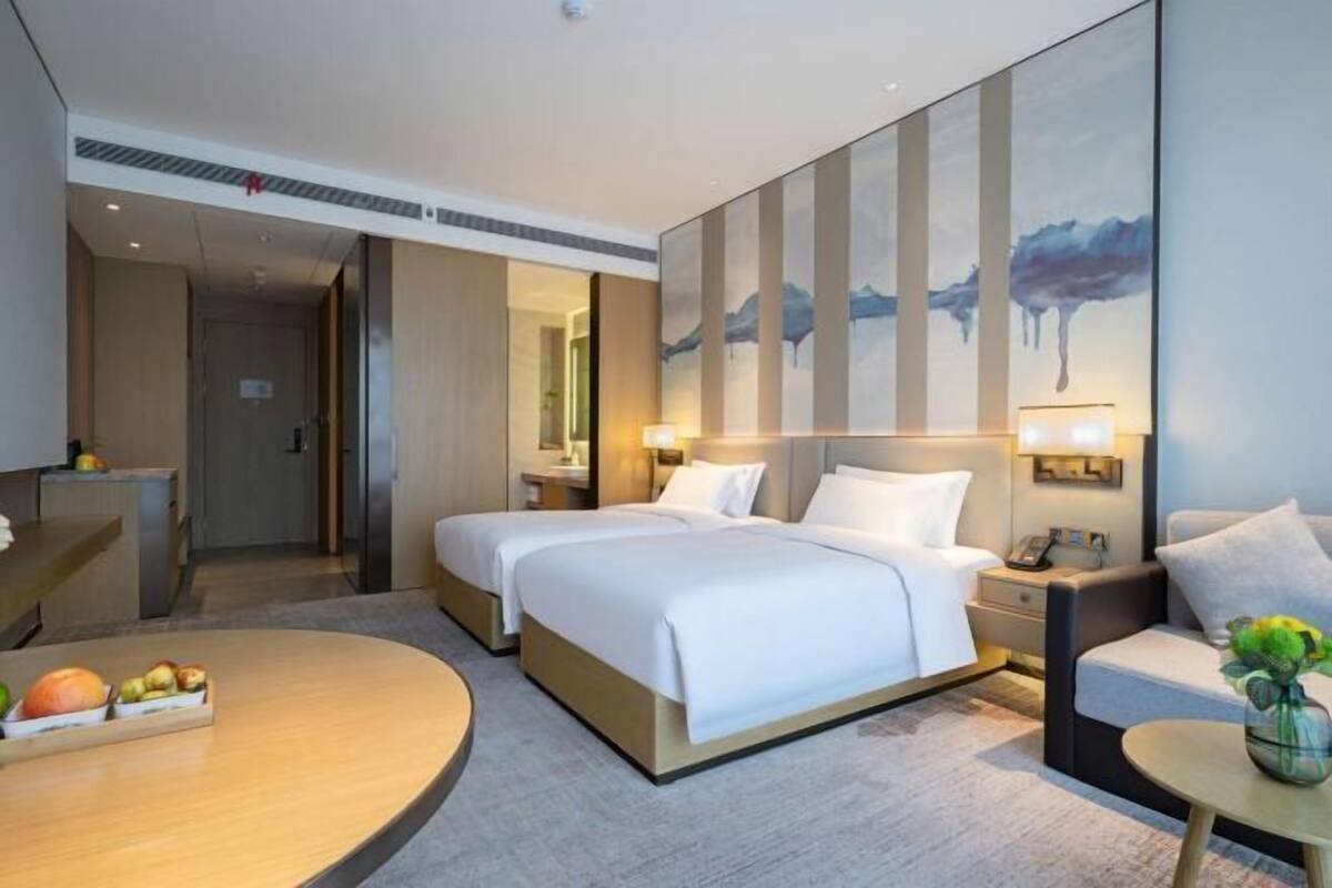 A hotel room with two beds, a sitting area, a dining table, and a large abstract painting on the wall.