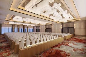 Un amplio salón de conferencias con filas de mesas y sillas, un diseño moderno en el techo y vistas a la ciudad.
