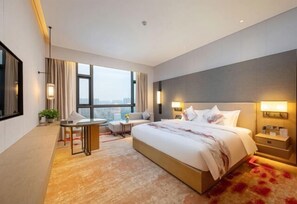 A hotel room with a large bed, a desk, a chair, and a view of the city. - Huake Xinyi Hotel (Zhuzhou)