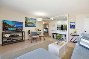 Una sala de estar con televisor, comedor, cocina y un pasillo que conduce a otra habitación.