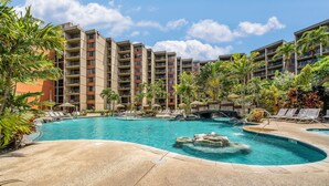 A hotel with a swimming pool, lounge chairs, and palm trees.