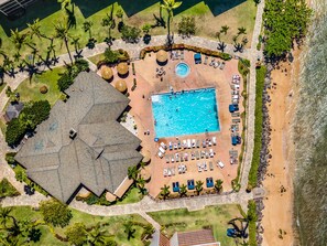 Vue aérienne d’un complexe hôtelier avec une piscine, des chaises longues et une plage.