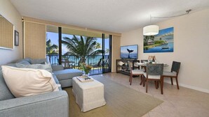 A spacious living room with a large window, a dining area with a table and chairs, and a sofa with a side table.