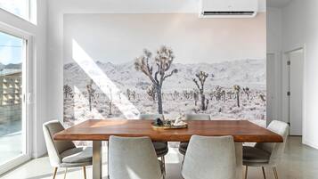 A dining area with a wooden table, four grey chairs, and a desert landscape mural on the wall.