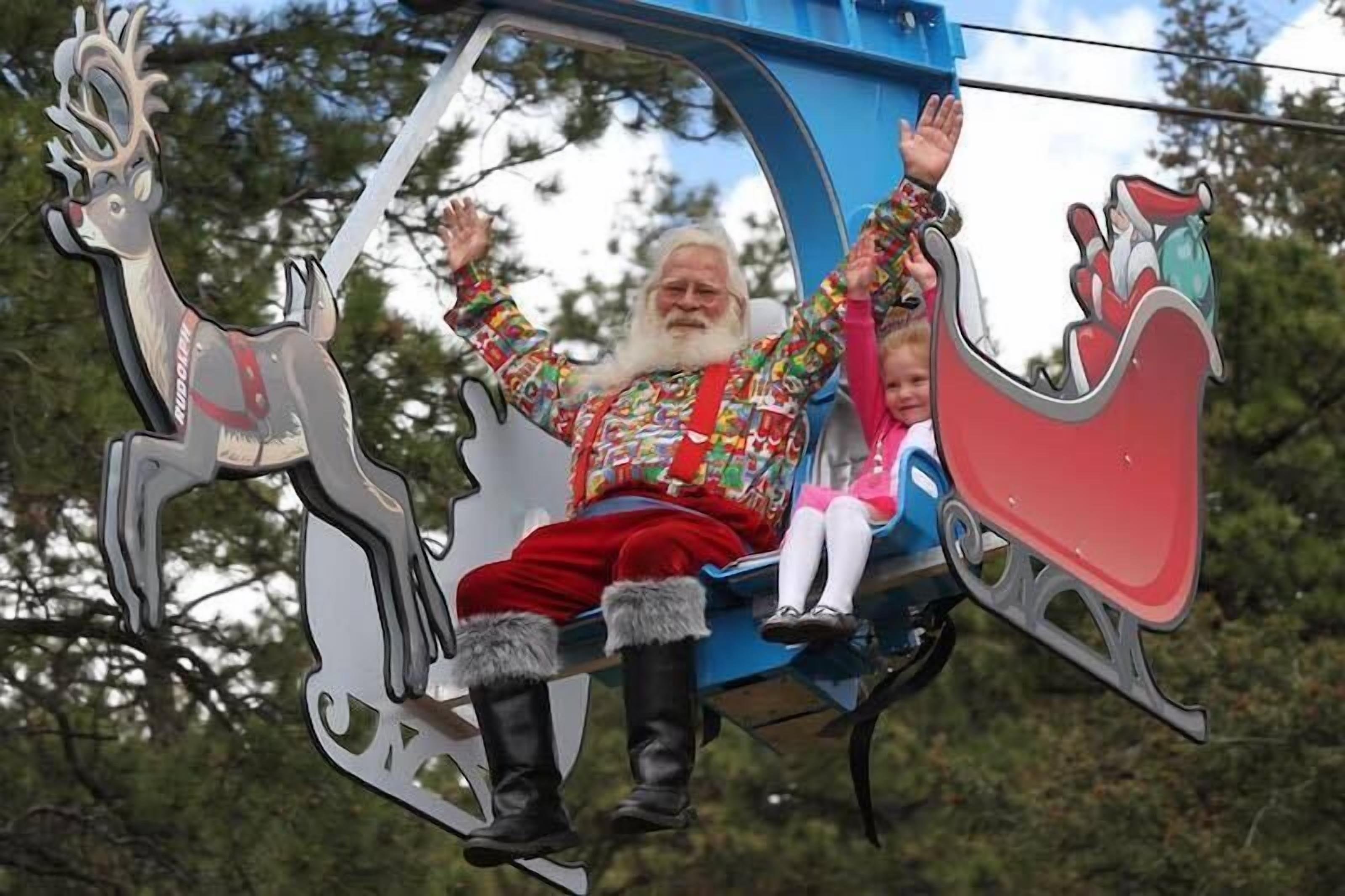 A person in a sleigh with reindeer decorations, a child, and a Santa Claus figure.