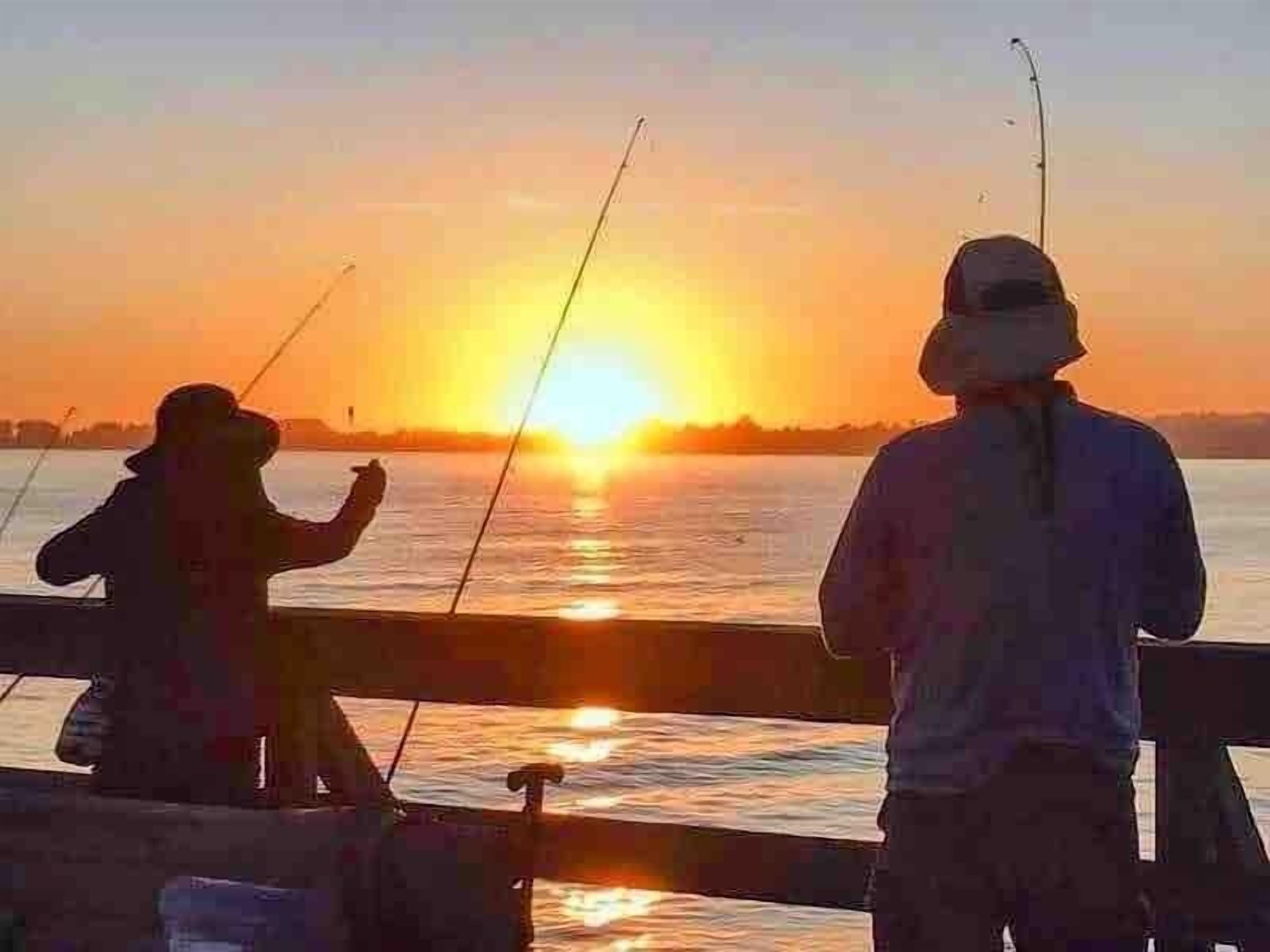 Two people fishing at sunset with the sun low on the horizon.