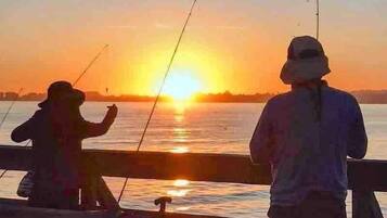 Two people fishing at sunset with the sun low on the horizon.