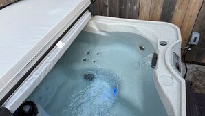 Jacuzzi con un colchón sumergido parcialmente en el agua, un panel de control y una cerca de madera al fondo.