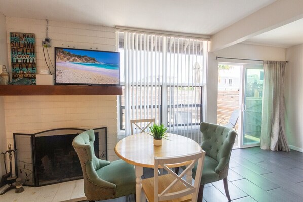 A living room with a fireplace, a television, and a large window with blinds.