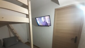 Huoneessa on kerrossänky, seinälle asennettu televisio ja puinen ovi.