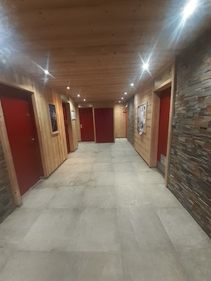 A hallway with wooden walls, red doors, and a stone accent wall. - Waala Centre Station Studio for 4 people (Les Deux Alpes)