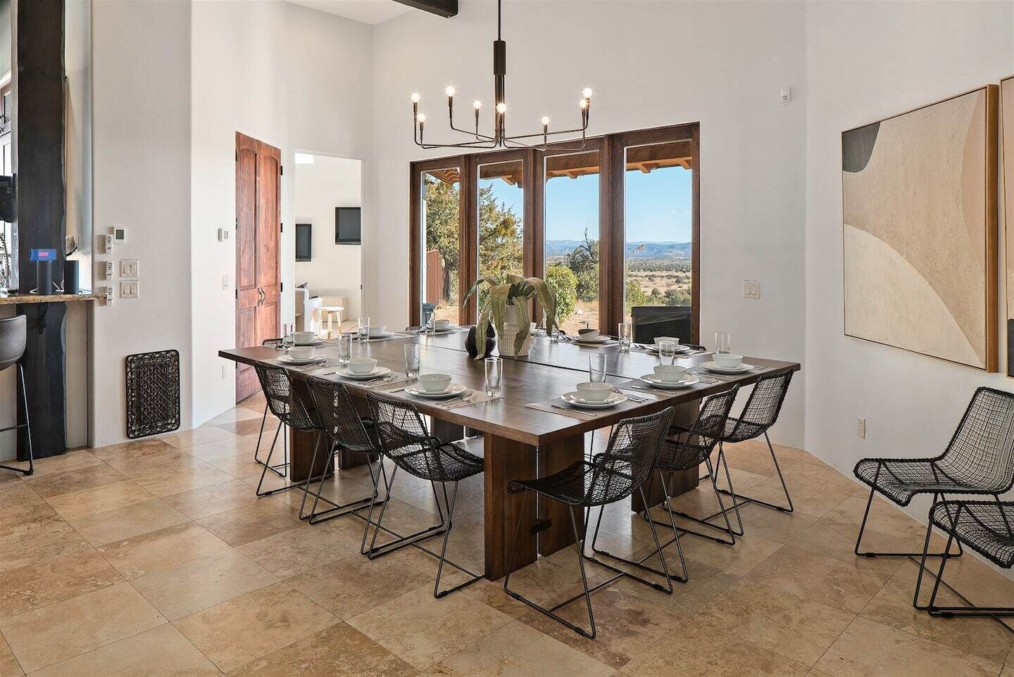 Un comedor amplio con una mesa larga, sillas de malla metálica negra y vistas al exterior a través de grandes ventanales.