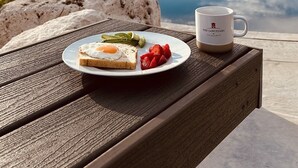 Ein Tisch mit Essen und einer Tasse, mit Blick auf eine Berglandschaft und ein Gewässer.