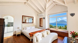 A bedroom with a bed, a nightstand, a dresser, a window with a view of the sea and a mountain, and a view of the kitchen. - Private Caribbean Cottage with Ocean & Nevis Views near Cockleshell Beach (Basseterre)