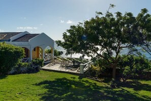 A coastal property with a white building, a wooden deck, and a large tree. - Private Caribbean Cottage with Ocean & Nevis Views near Cockleshell Beach (Basseterre)