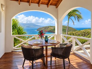 A wooden deck with a table and chairs, overlooking a coastal landscape with a view of the ocean and hills. - Private Caribbean Cottage with Ocean & Nevis Views near Cockleshell Beach (Basseterre)