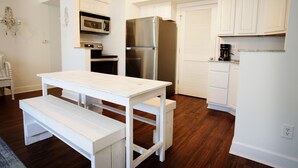 Una cocina con armarios blancos, un refrigerador de acero inoxidable, un microondas y una mesa de comedor blanca con bancos.