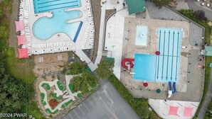 Ovenfra ses et hotel med flere swimmingpools, udendørs siddeområder og en anlagt have.