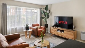 A modern living room with a large flat-screen TV, a brown leather sofa, a small round coffee table, and a potted plant. - Modern Luxurious Living With Your Own Parking Spot (Sandy Bay)