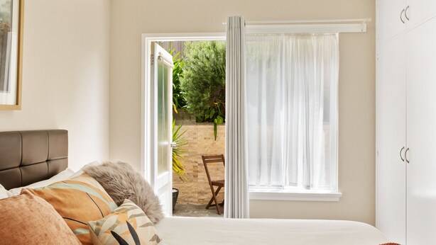 A bedroom with a bed, a window with curtains, a chair, and a view of an outdoor area. - Modern Luxurious Living With Your Own Parking Spot (Sandy Bay)