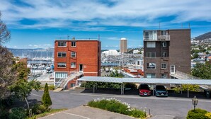 A parking area with two buildings, one red and one brown, and a marina in the background. - Modern Luxurious Living With Your Own Parking Spot (Sandy Bay)