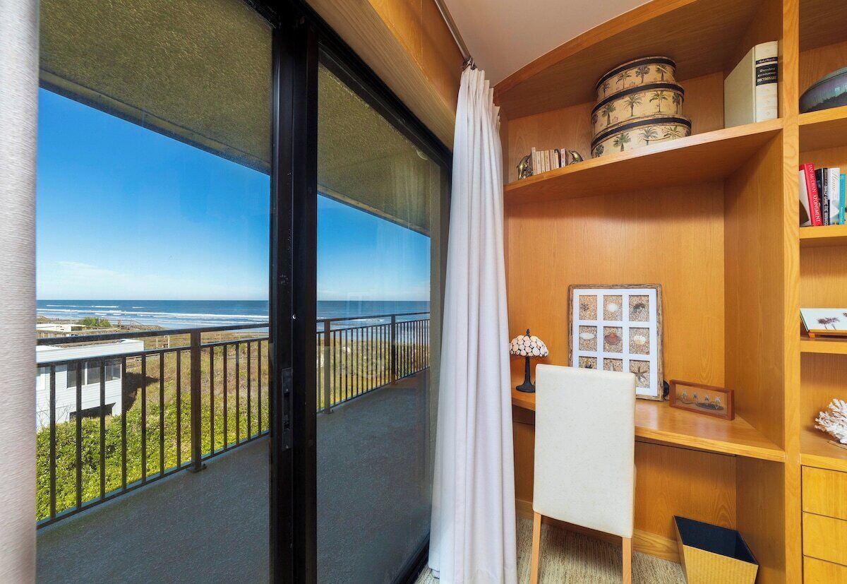 A balcony with a view of the ocean, a desk with a lamp, and shelves with decorative items.