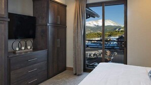Une chambre dotée d’un grand lit, d’une armoire en bois foncé, d’un téléviseur à écran plat et offrant une vue sur un paysage montagneux enneigé, visible à travers une porte-fenêtre coulissante.