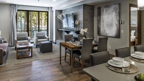 Une chambre d’hôtel moderne dotée d’un coin repas, d’un ensemble de canapés, d’un téléviseur fixé au mur et d’un grand tableau abstrait.