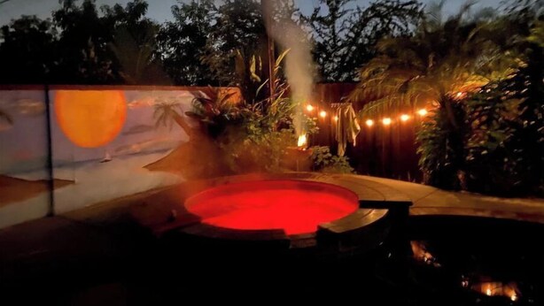 A hot tub with a red glow, surrounded by trees and a mural of a sunset. - Great 3 bedroom 2 bath single family home close to Disneyland. (Brea)