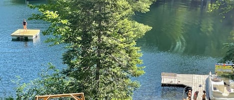 A wooden dock extending into a lake, surrounded by lush greenery and a swing chair.