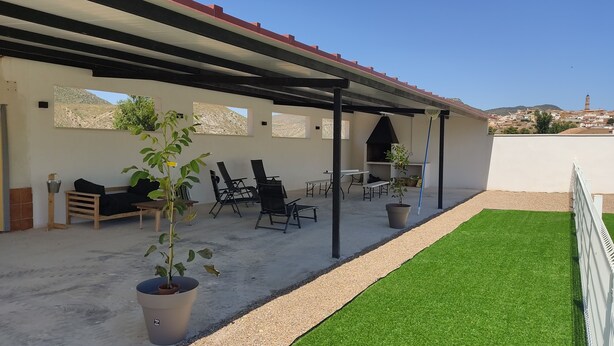 Une terrasse extérieure dotée d’un espace salon couvert, d’une petite pelouse et d’une vue sur une ville située au loin.