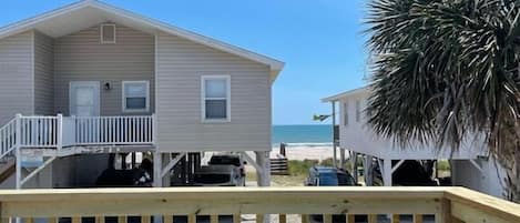 A beach house with a balcony, two Adirondack chairs, and a view of the ocean.