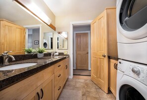 Un baño moderno con lavamanos de encimera de granito, armarios de madera, un espejo grande y lavadora y secadora apiladas.